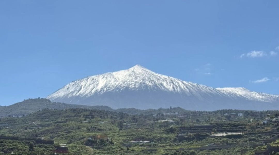 Ośnieżony szczyt Teide na Teneryfie widoczny nad zielonymi dolinami i tarasami uprawnymi.
