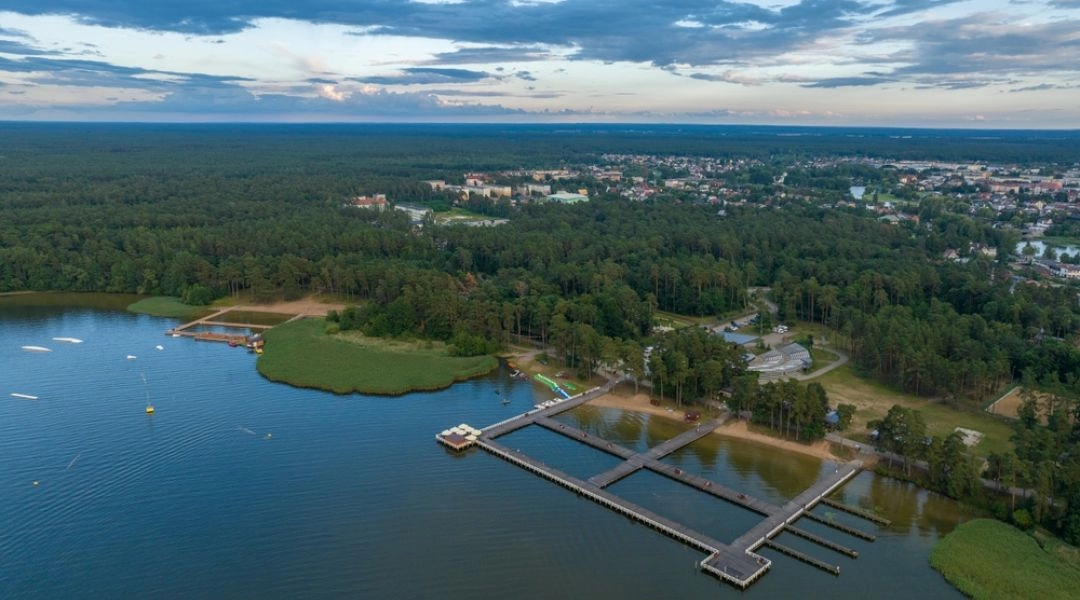 Jezioro Necko w Augustowie widziane z lotu ptaka, z pomostami, plażą i lasem przy brzegu.