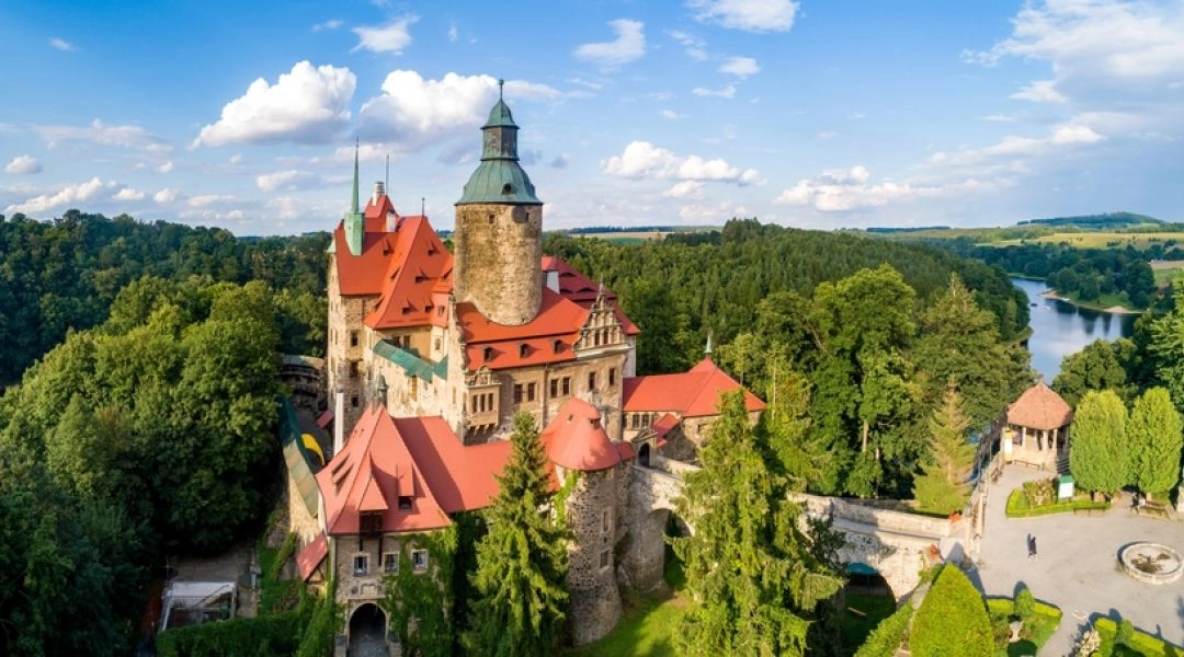 Zamek Czocha sfotografowany z góry, z czerwonymi dachami, mostem wjazdowym i Jeziorem Leśniańskim w tle.