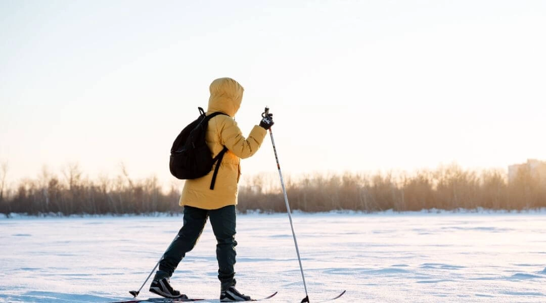 Osoba biegnąca na nartach biegowych po zaśnieżonym, otwartym terenie zimą.