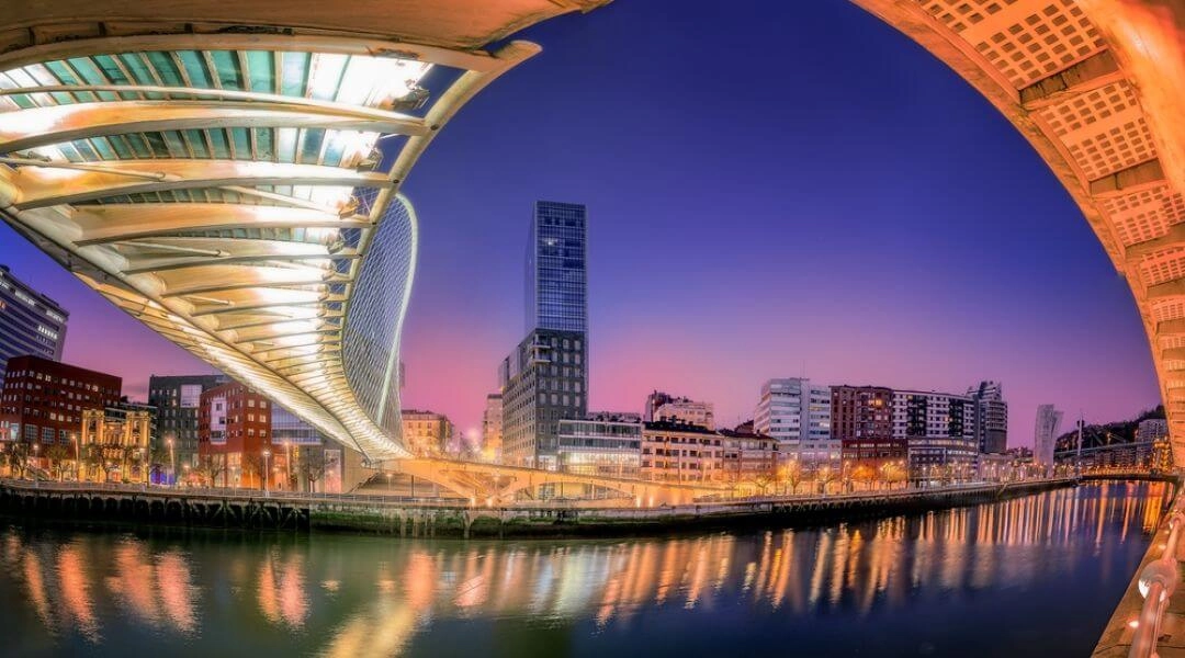 Nowoczesny most Zubizuri nad rzeką Nervión i panorama Bilbao o zachodzie słońca.
