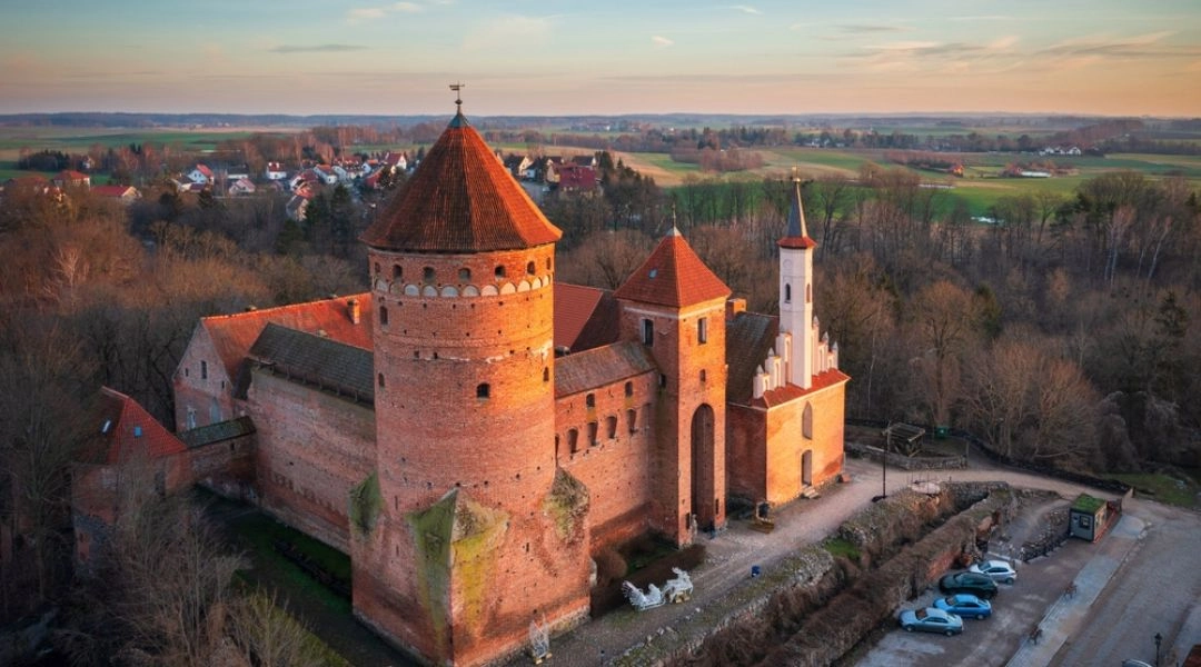 Gotycki Zamek w Reszlu sfotografowany z lotu ptaka, z ceglaną wieżą i zabudową miasteczka w tle.