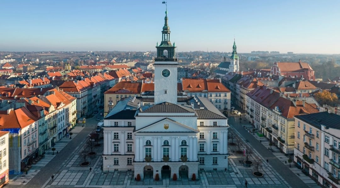 Widok z góry na ratusz i Główny Rynek w Kaliszu z kamienicami oraz kościołami w tle.