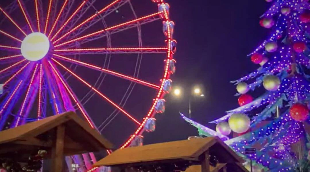 Jarmark świąteczny przed Pałacem Kultury i Nauki w Warszawie z podświetlonym diabelskim młynem wieczorem.