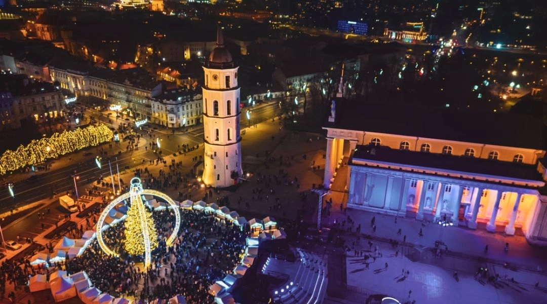 Jarmark bożonarodzeniowy w Wilnie nocą. Widok z lotu ptaka na rozświetloną choinkę, świąteczne stoiska, dzwonnicę i katedrę na placu Katedralnym.
