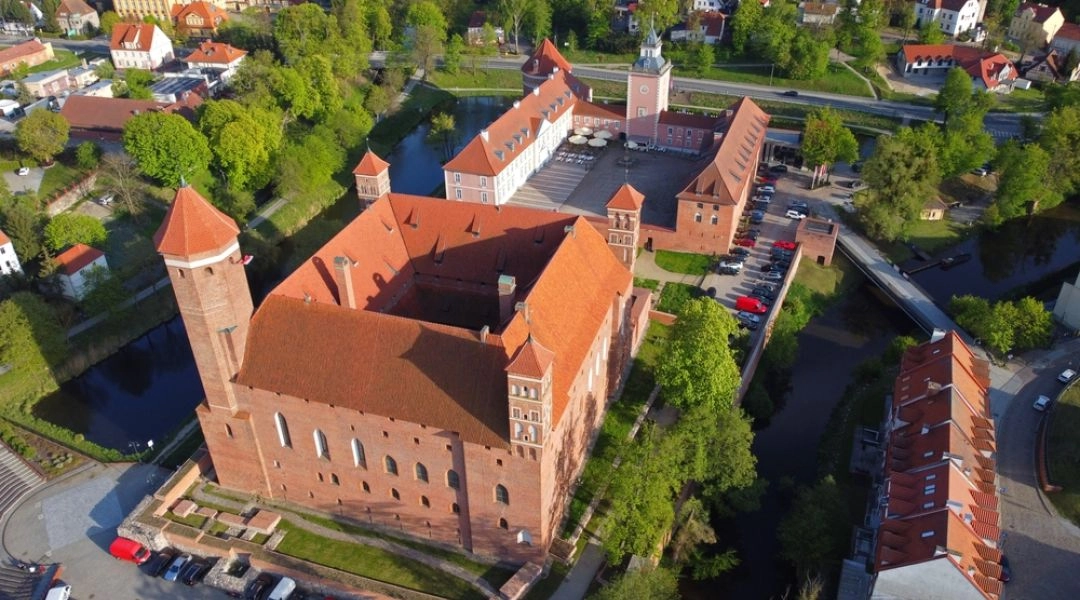 Lotnicze ujęcie gotyckiego Zamku Biskupów Warmińskich w Lidzbarku Warmińskim otoczonego fosą.
