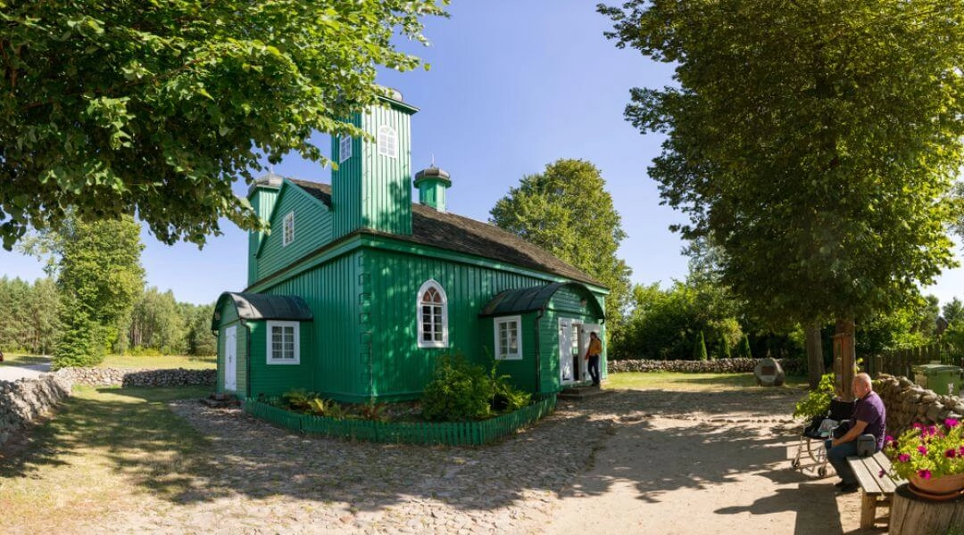 Zielony drewniany meczet w Kruszynianach stojący wśród drzew przy brukowanej drodze.