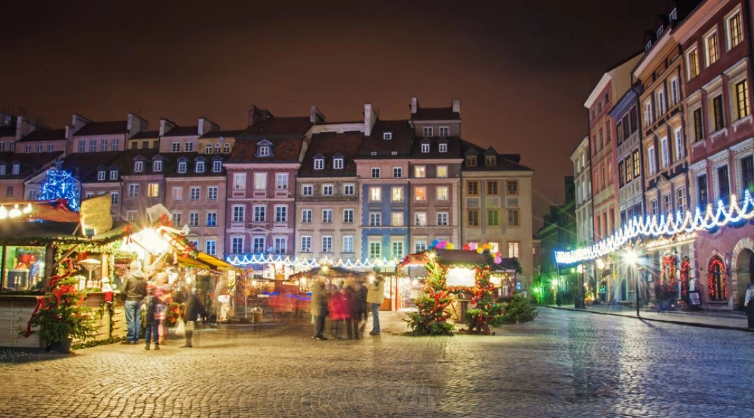 Jarmark bożonarodzeniowy na Rynku Starego Miasta w Warszawie z drewnianymi stoiskami i świątecznymi dekoracjami.