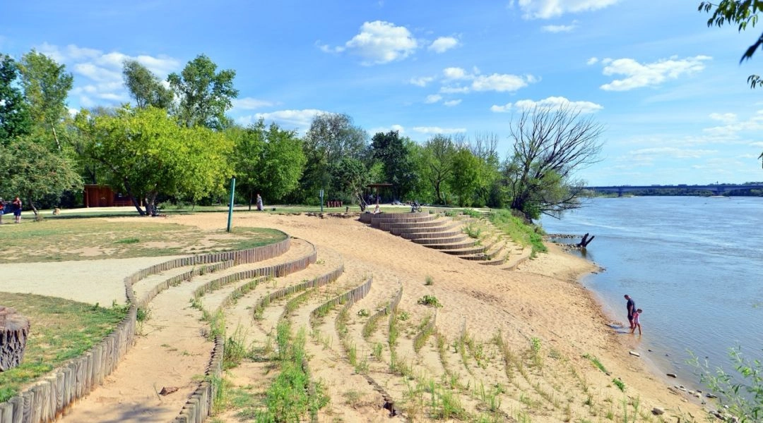 Tarasowo urządzona Plaża Romantyczna w Warszawie z drewnianymi schodami, zielenią i brzegiem Wisły.