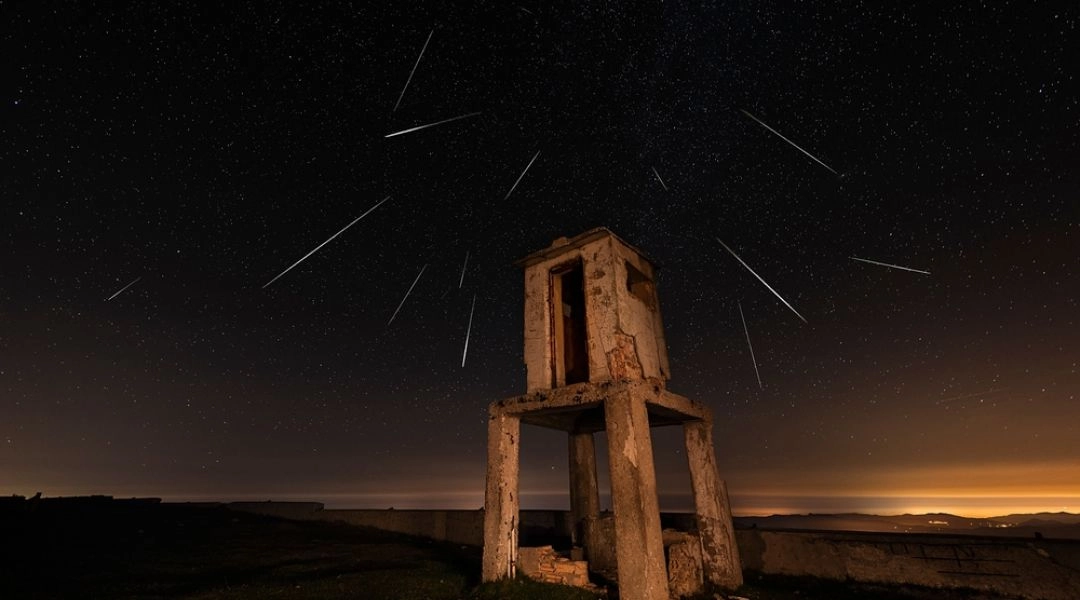 Smugi Perseidów na nocnym niebie nad opuszczoną kamienną budowlą