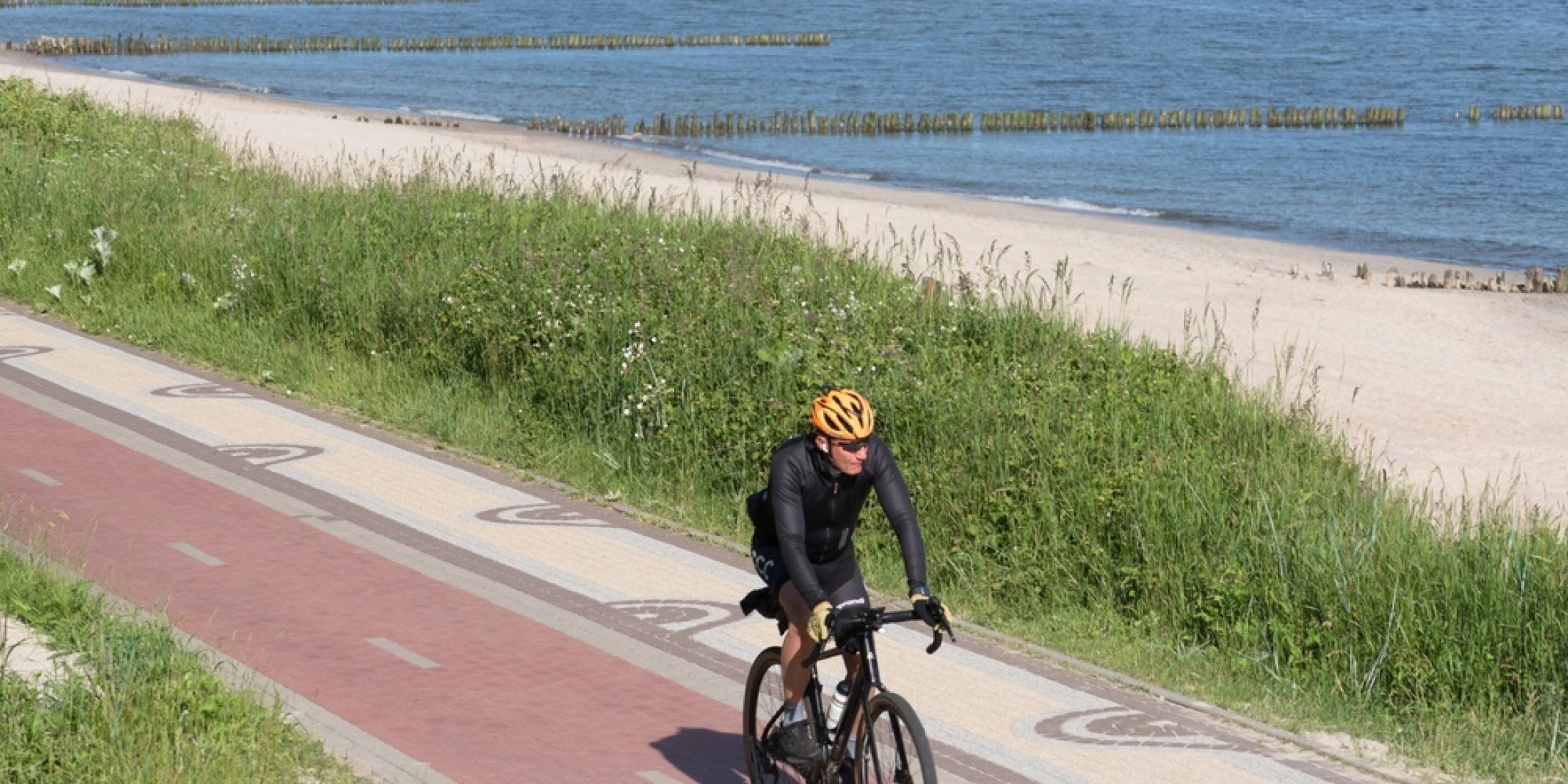 Rowerzysta jadący nadmorską trasą rowerową wzdłuż piaszczystej plaży i Bałtyku.