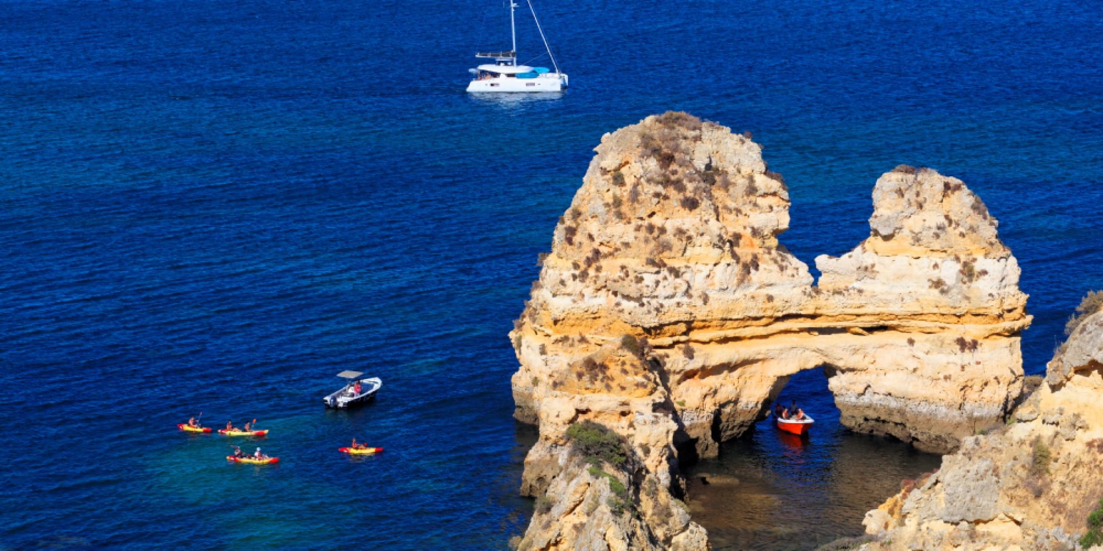 Formacje skalne Ponta da Piedade na wybrzeżu Algarve, kajaki i jacht na Atlantyku, błękitne morze, statek w tle