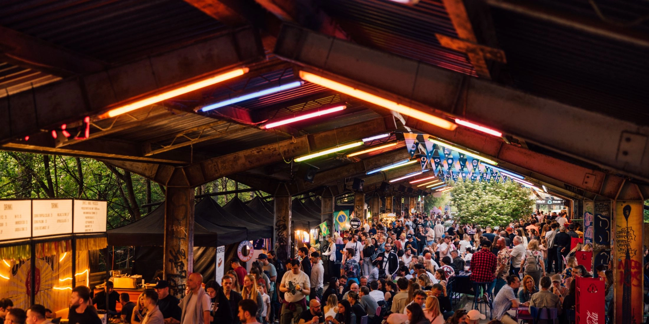 Wieczorny widok na Nocny Market z tłumem gości, kolorowymi neonami i stoiskami gastronomicznymi pod zadaszeniem dawnych peronów.