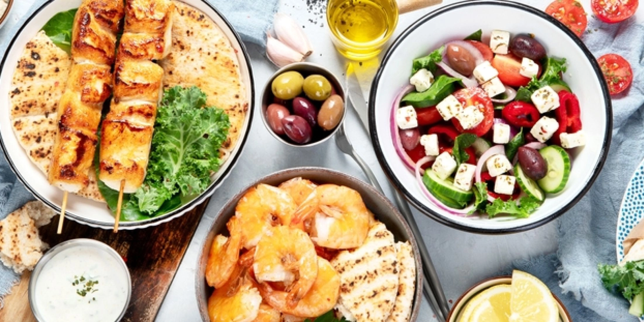 Grecka kuchnia i przekąski na stole: souvlaki, krewetki, sałatka grecka z fetą, oliwki i pita