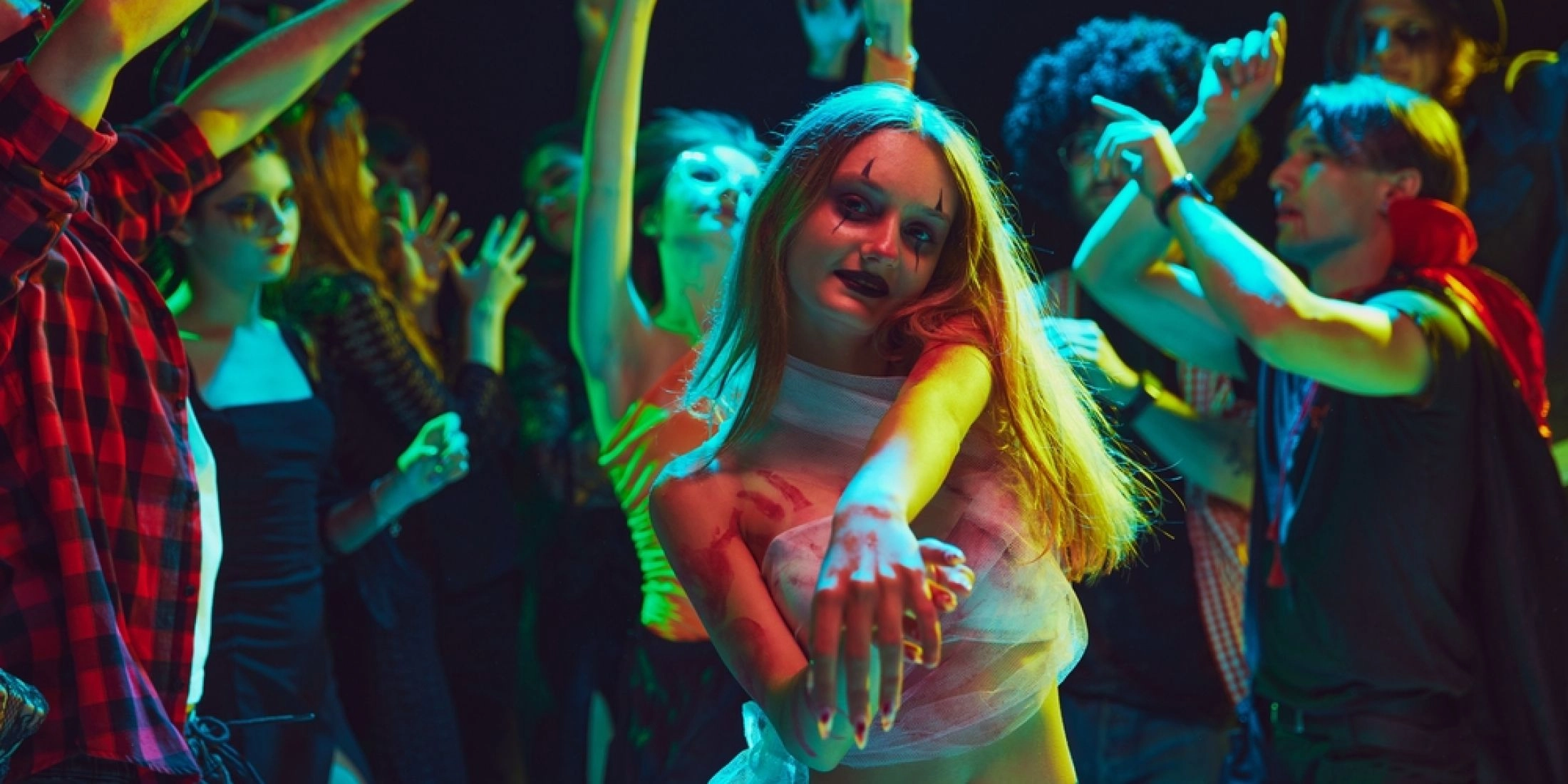 Kobieta z halloweenowym makijażem i bandażami imitującymi strój mumii tańczy w klubie wśród uczestników imprezy.