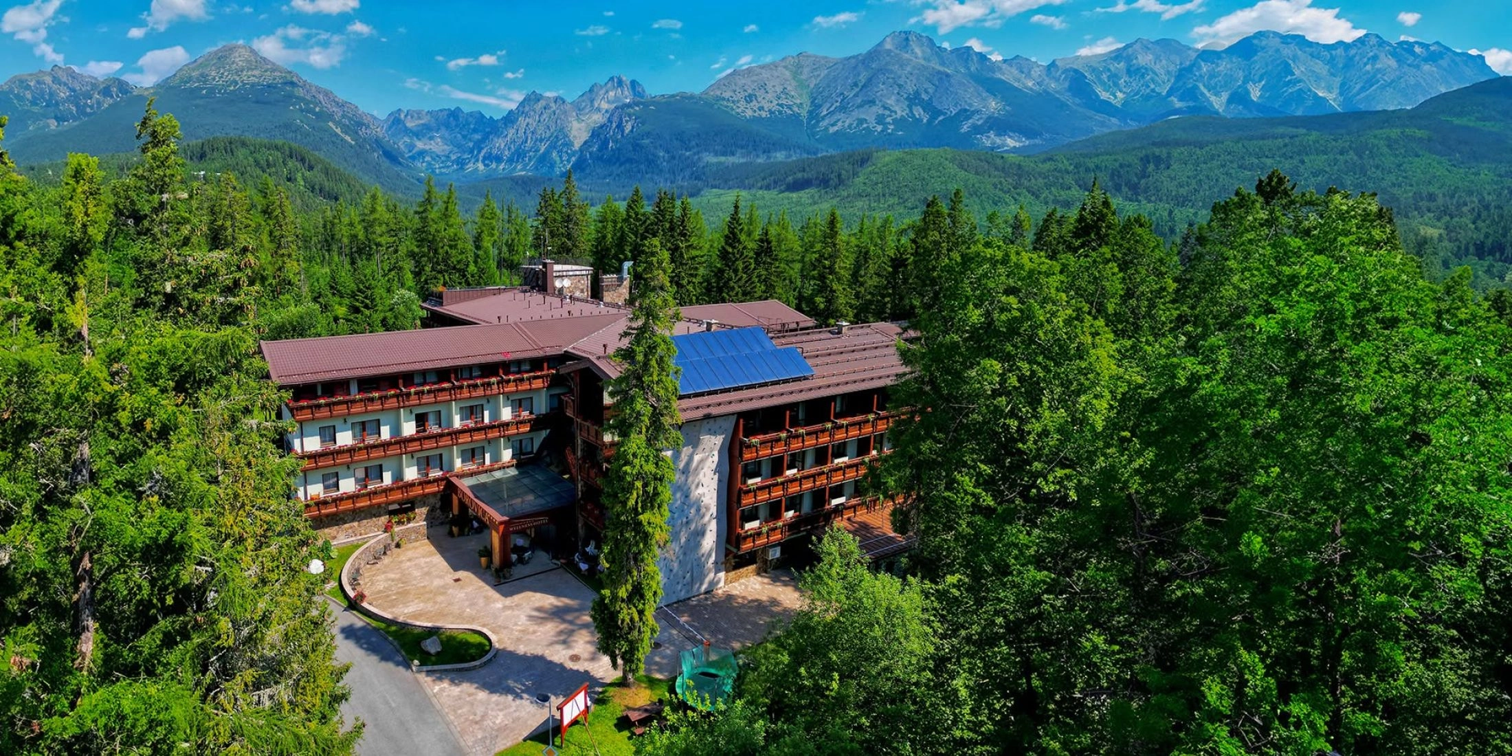 Hotel Borovica położony wśród lasów Štrbskiego Plesa na tle panoramy Tatr Wysokich.