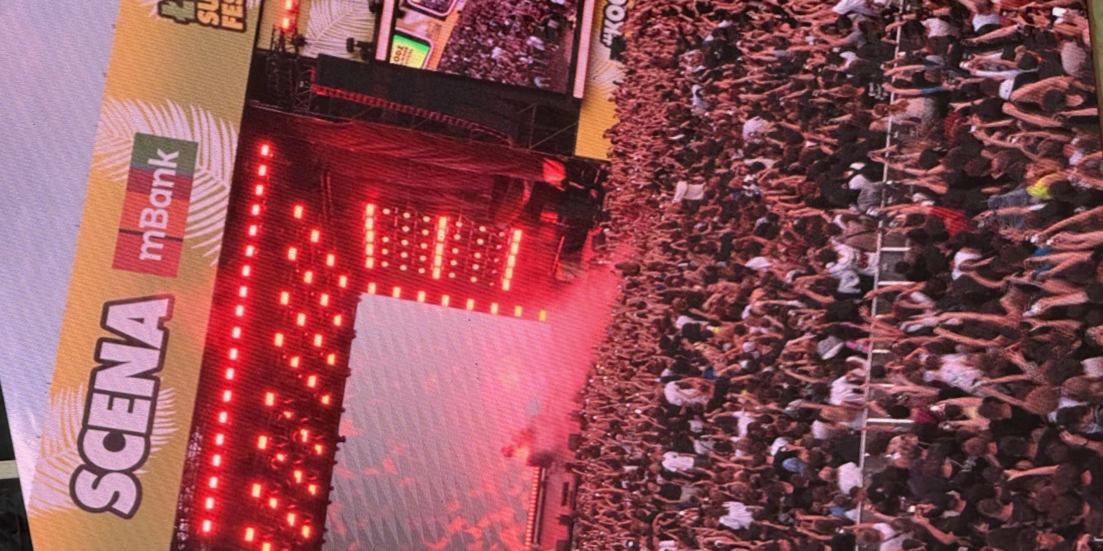 Artysta występujący na czerwono oświetlonej scenie Łódź Summer Festival przed tłumem publiczności.