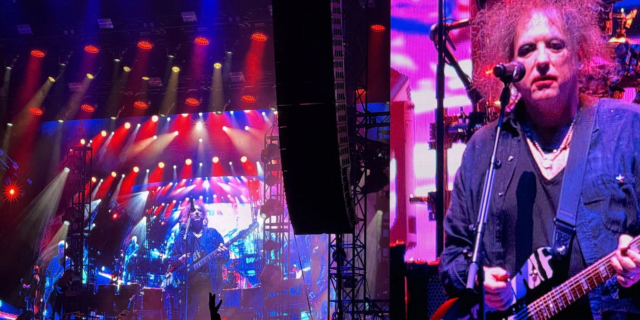 Koncert The Cure na festiwalu Pohoda, scena oświetlona czerwonym i niebieskim światłem, a na wielkim ekranie wokalista grający na gitarze.