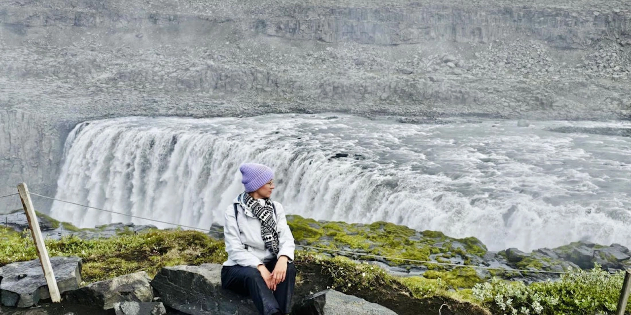 Autorka siedząca na skałach przy potężnym wodospadzie Dettifoss na Islandii.