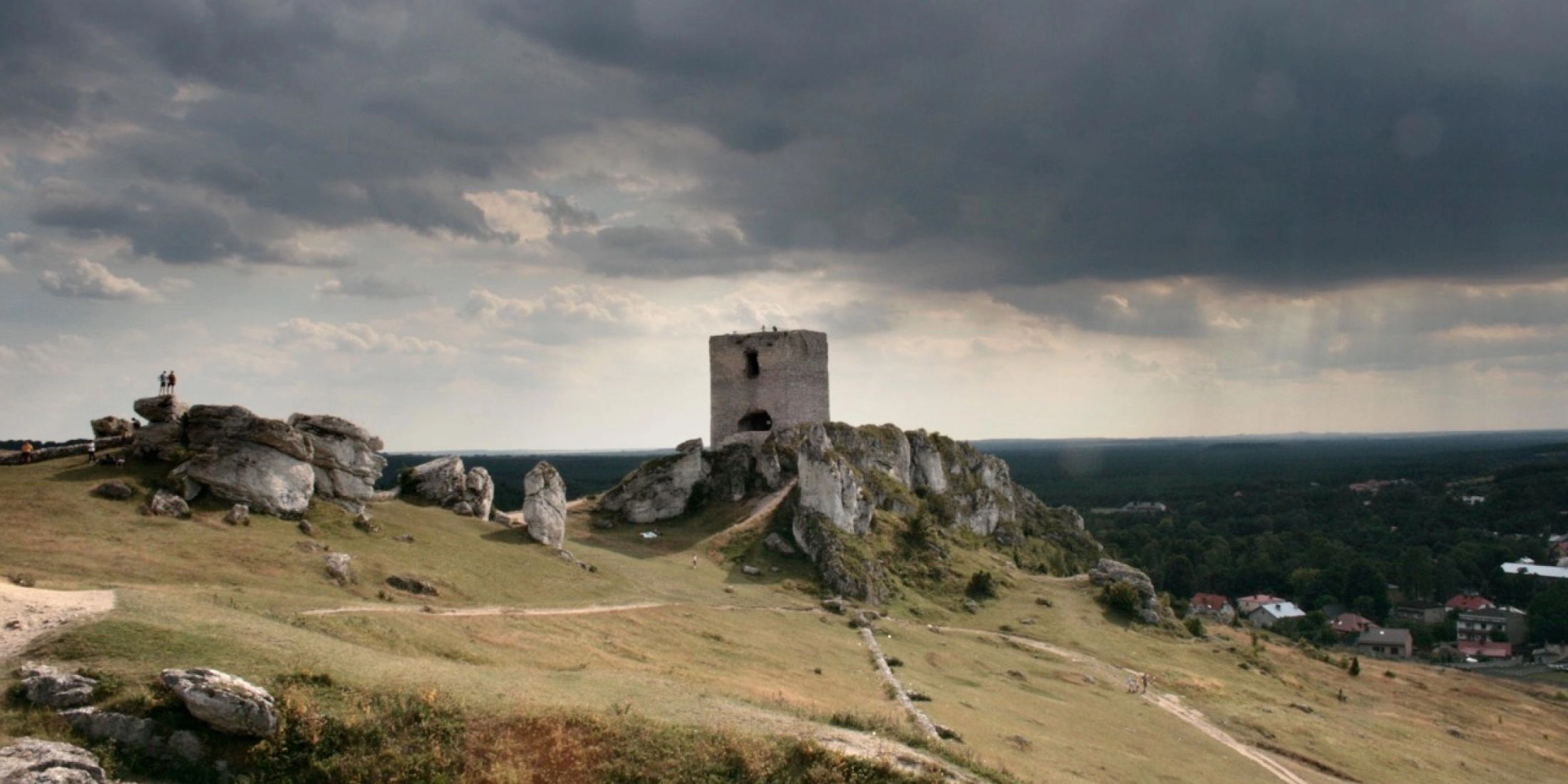 Kamienna wieża zamku w Olsztynie wznosząca się na wapiennej grani pod burzowym niebem.