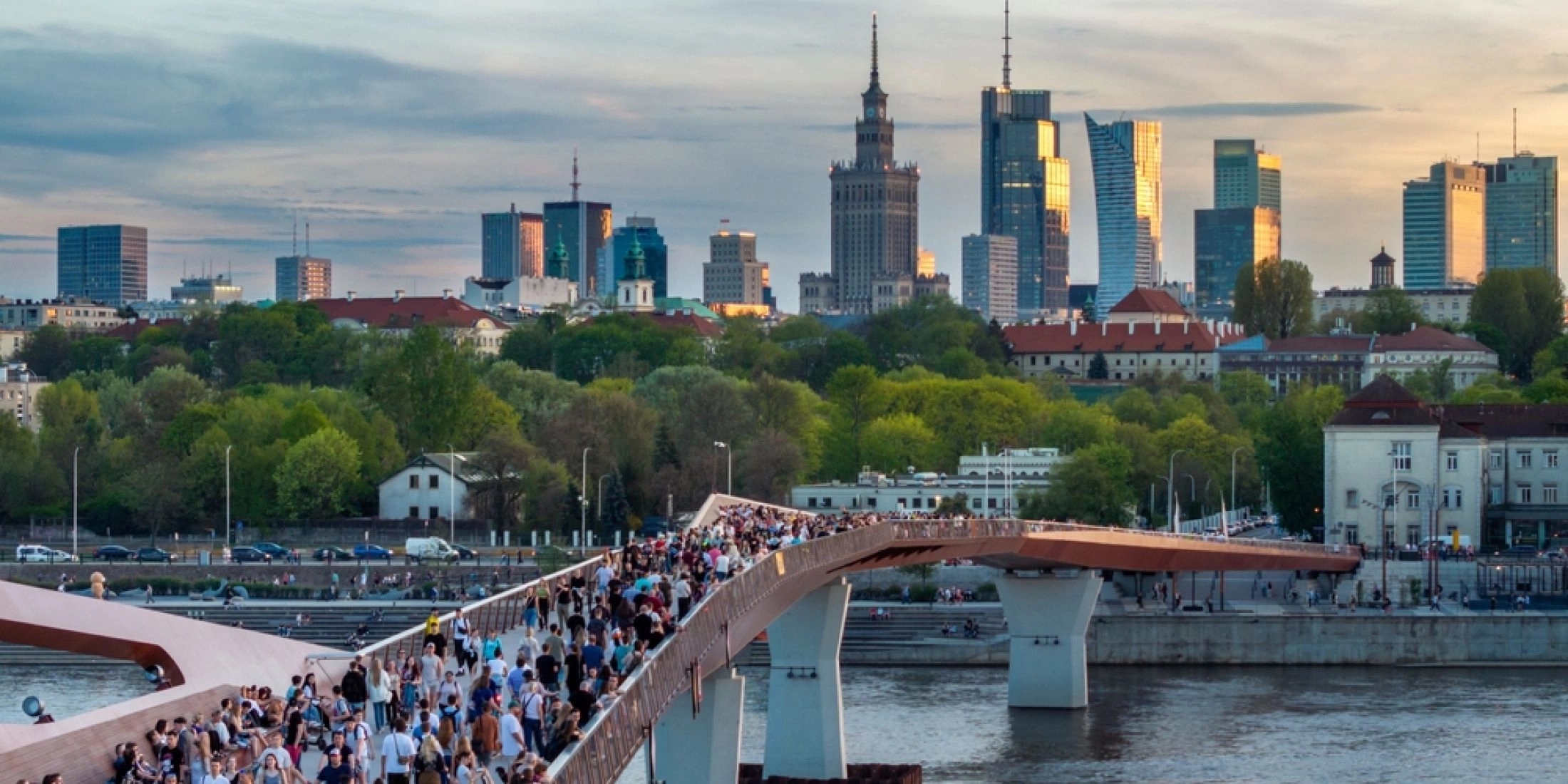 Kładka pieszo-rowerowa nad Wisłą w Warszawie z dużą liczbą spacerujących osób.