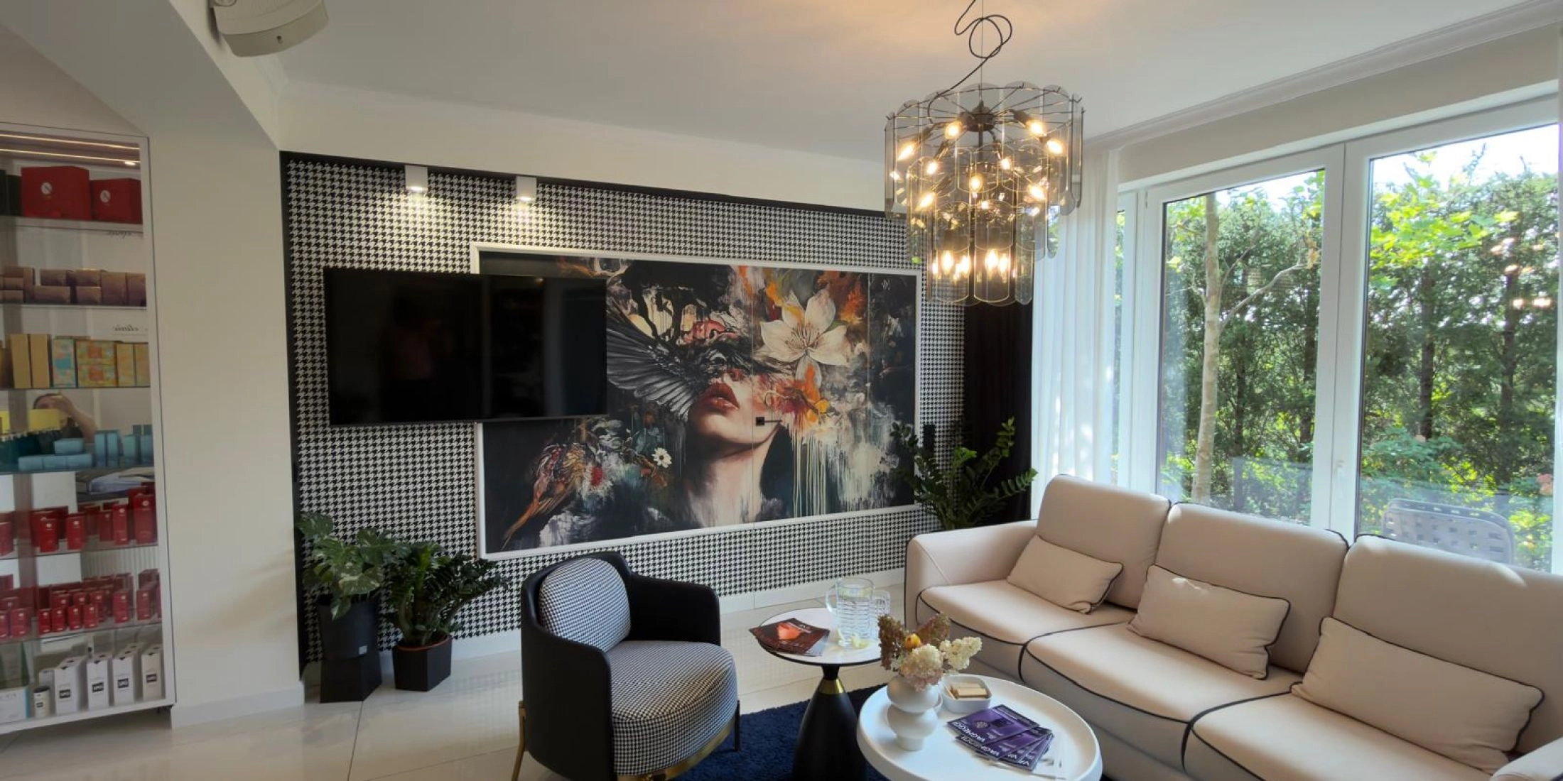 Jasna sofa i fotel w pepitkę przy stolikach, na tle ściany z portretem kobiety i dużych okien wychodzących na ogród.