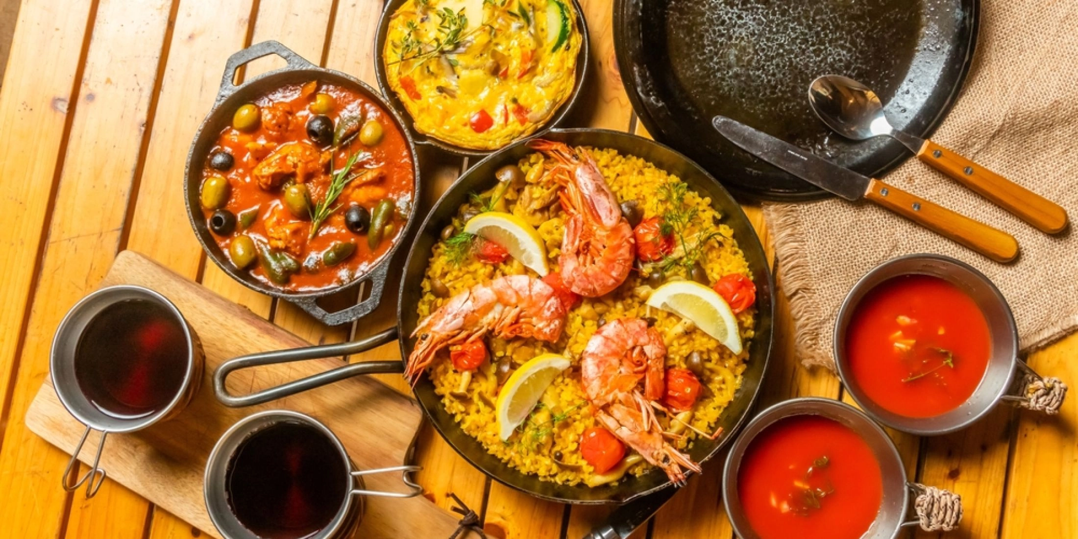 Paella z krewetkami, tapas z oliwkami i dwa kieliszki czerwonego wina na drewnianym stole