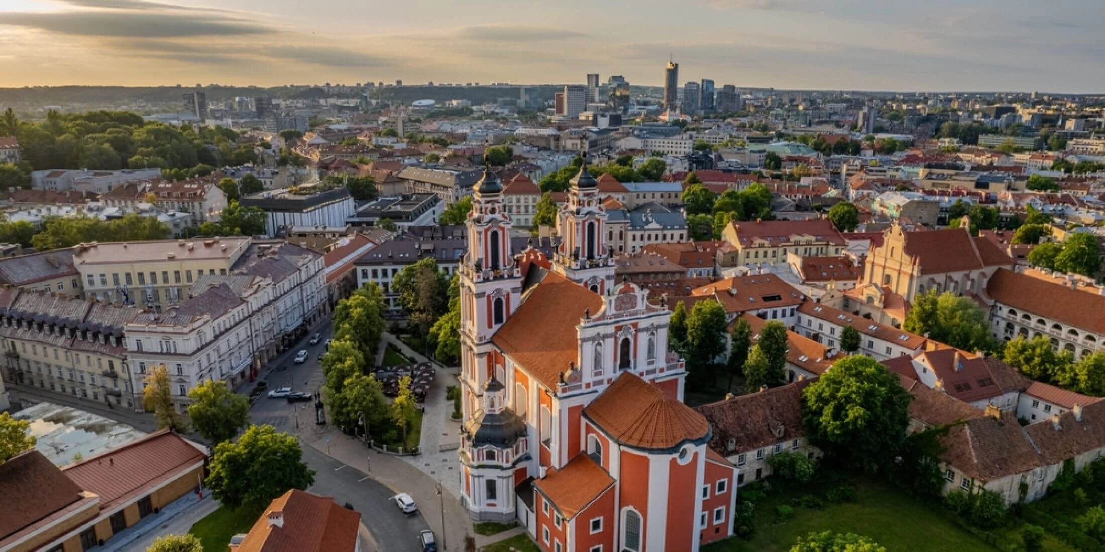 Panorama Wilna z lotu ptaka z kościołem św. Katarzyny, czerwonymi dachami Starego Miasta i wieżowcami w oddali.