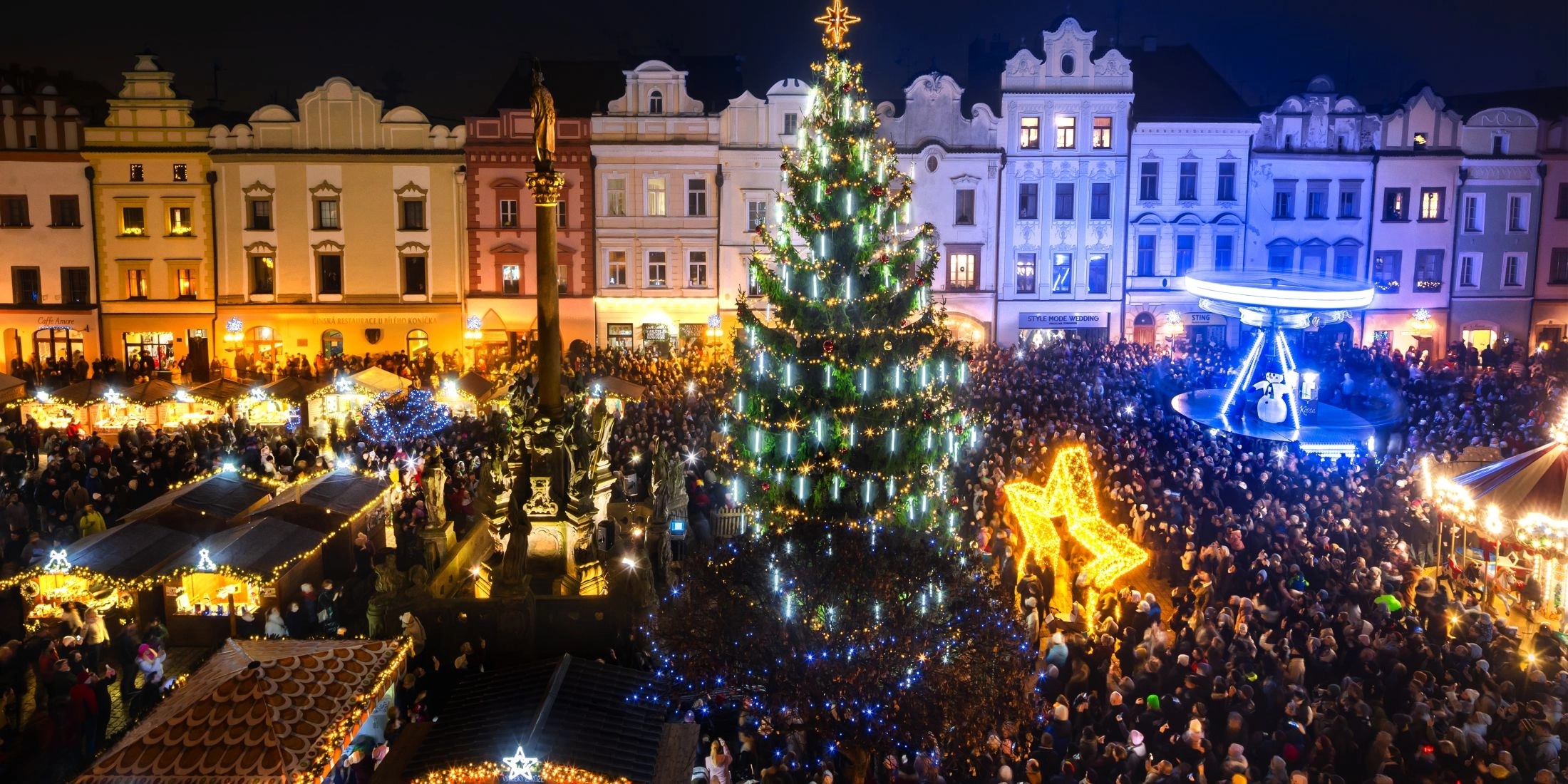 Tłum ludzi zgromadzonych wokół wielkiej udekorowanej choinki i świątecznych straganów na Placu Perštýnskim w Pardubicach.