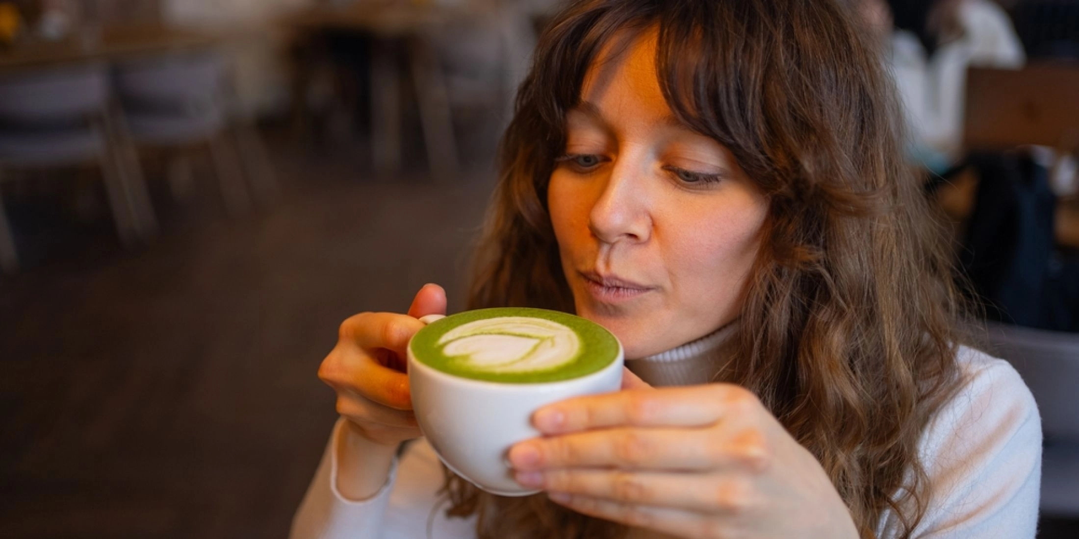 Kobieta pije matcha latte z charakterystyczną zieloną pianką w kawiarni.