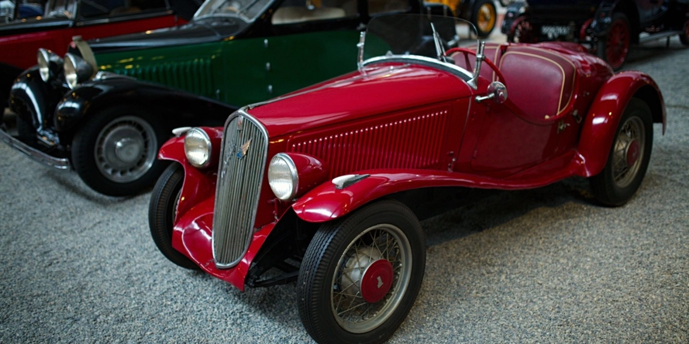 Czerwony zabytkowy samochód sportowy z lat 20. XX wieku na ekspozycji Narodowego Muzeum Motoryzacji w Miluzie, prezentowany wśród klasycznych europejskich modeli.