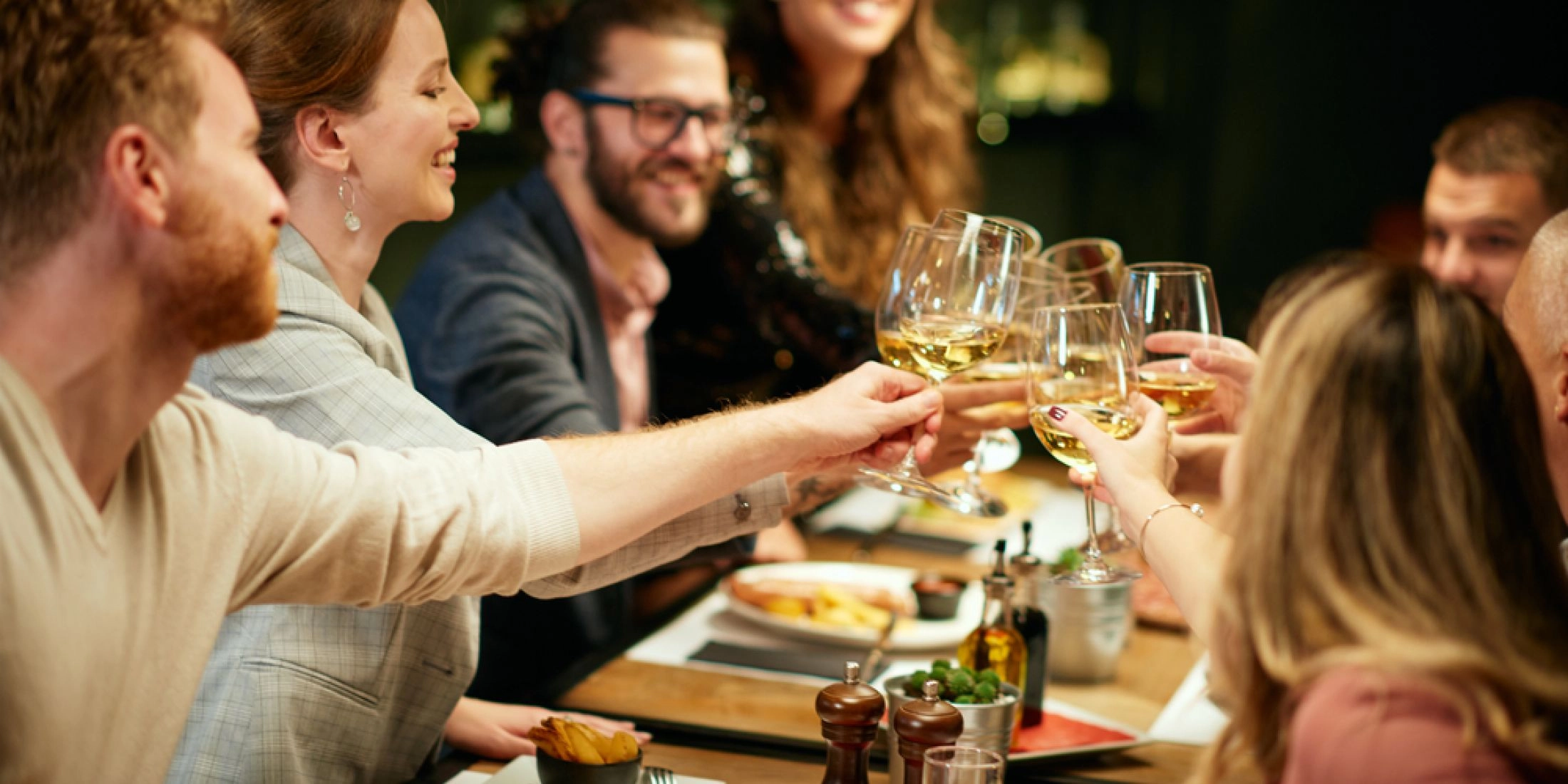 Grupa znajomych wznosząca toast kieliszkami wina podczas kolacji w restauracji.