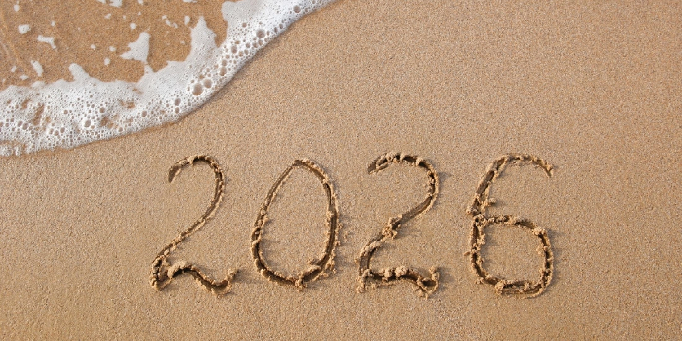 Napis 2026 na piasku nad brzegiem morza symbolizujący podróże.