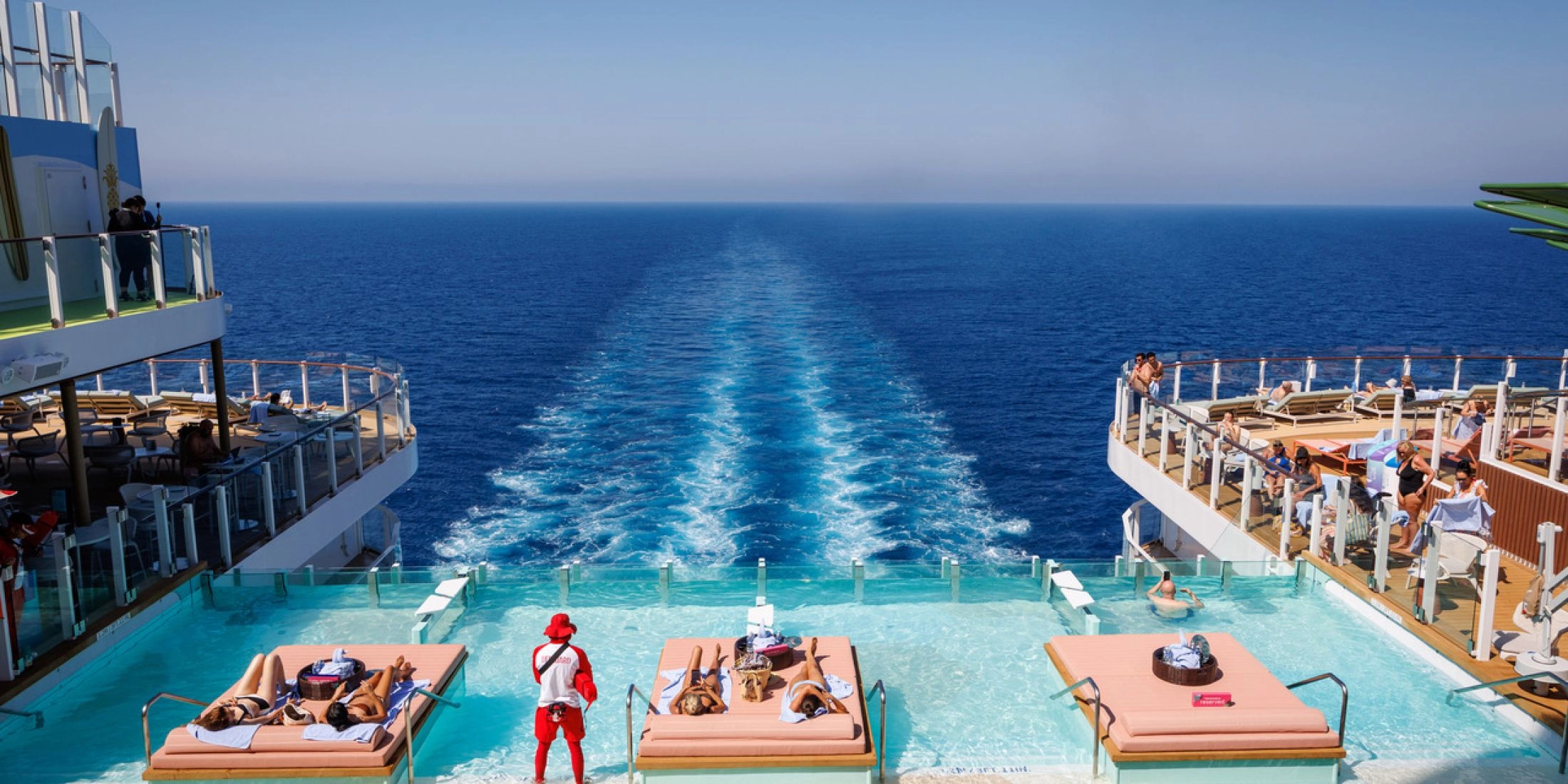 Błękitny basen infinity w strefie The Hideaway na rufie Legend of the Seas, z leżankami ustawionymi w wodzie i widokiem na morze oraz ratownikiem stojącym w wodzie.