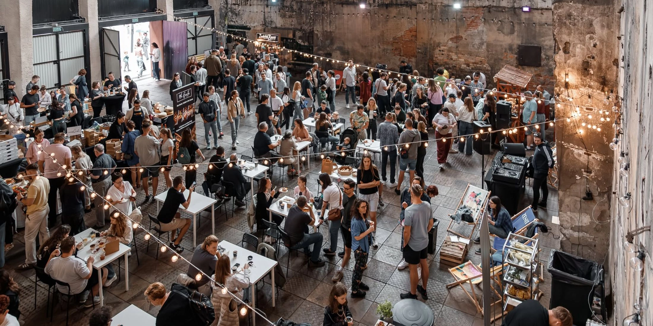 Tłum ludzi przy stolikach i stoiskach gastronomicznych w industrialnym wnętrzu dawnej fabryki