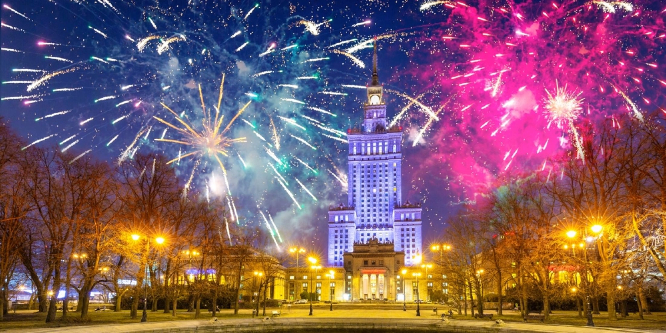 Pałac Kultury i Nauki w Warszawie nocą z kolorowymi fajerwerkami na niebie.