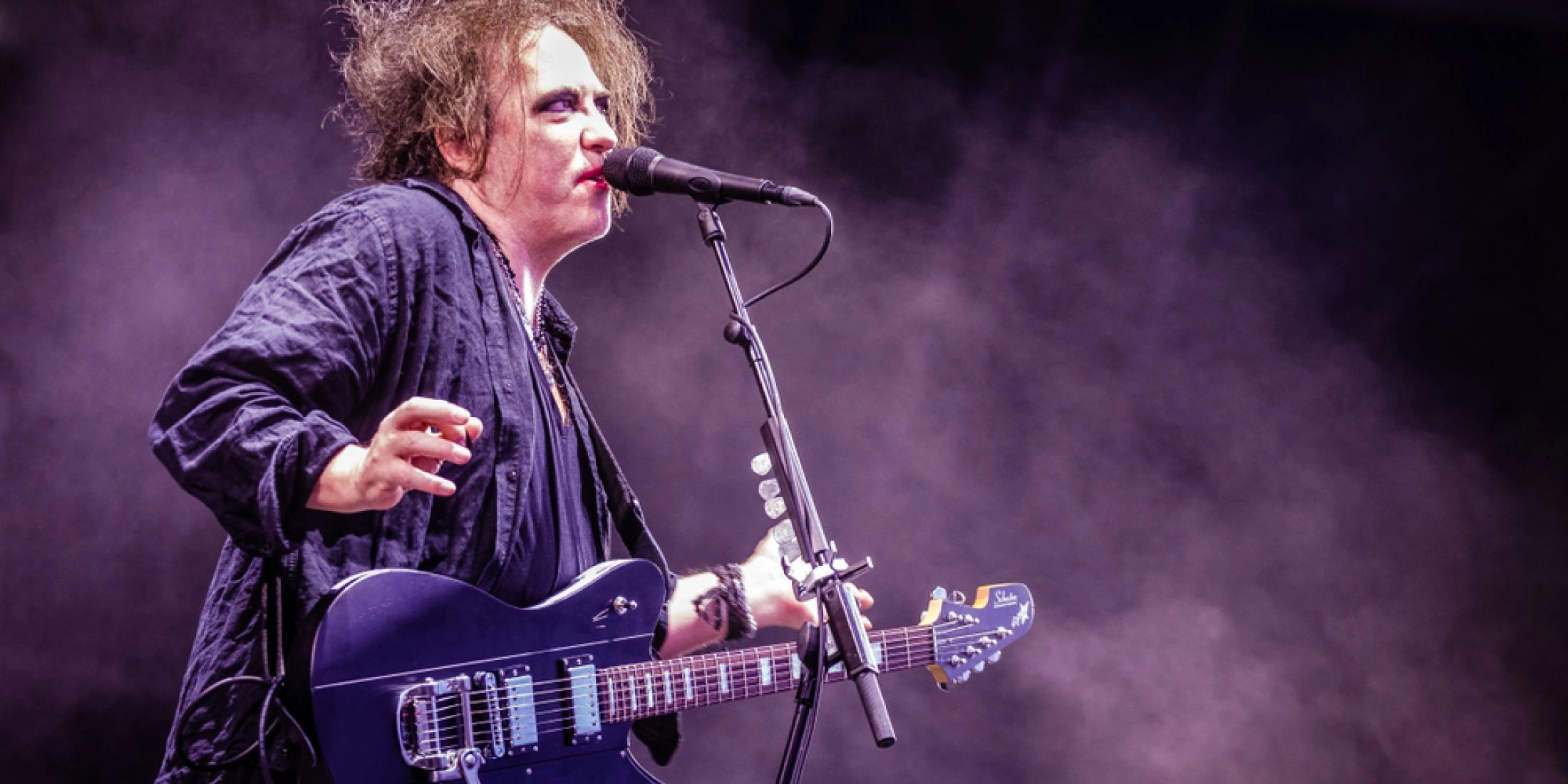 Wokalista The Cure śpiewa i gra na gitarze podczas koncertu