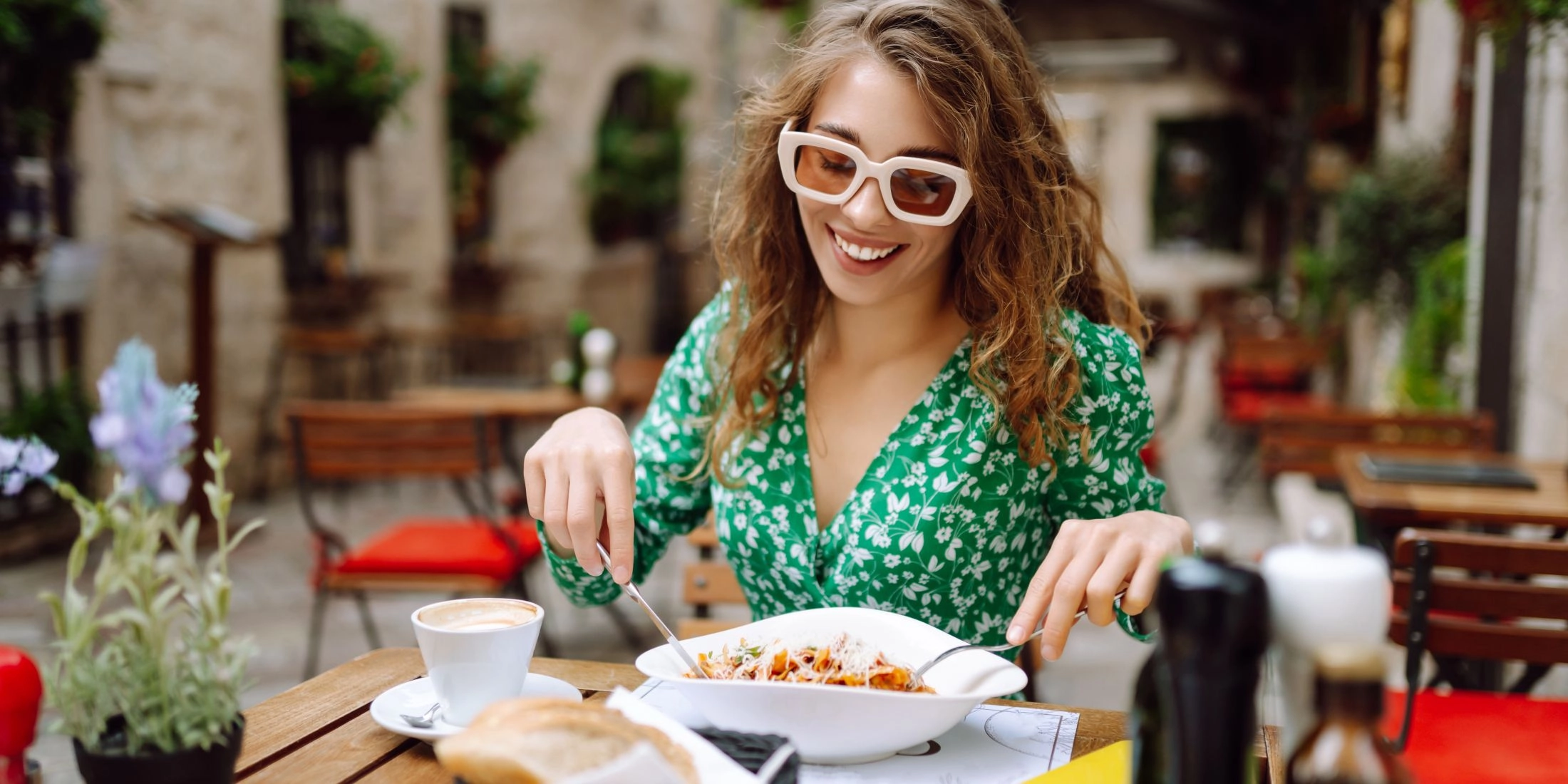 Kobieta siedzi przy stoliku w restauracyjnym ogródku i je makaron podczas kulinarnej podróży po Europie.