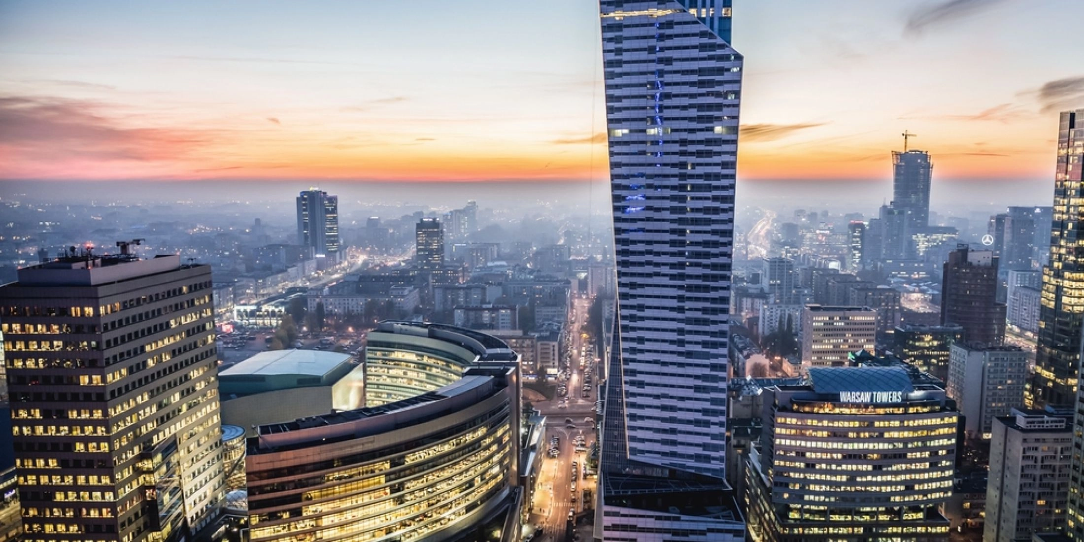 Warszawa z lotu ptaka o zmierzchu, skyline z wieżowcem Złota 44 i światłami miasta w tle.