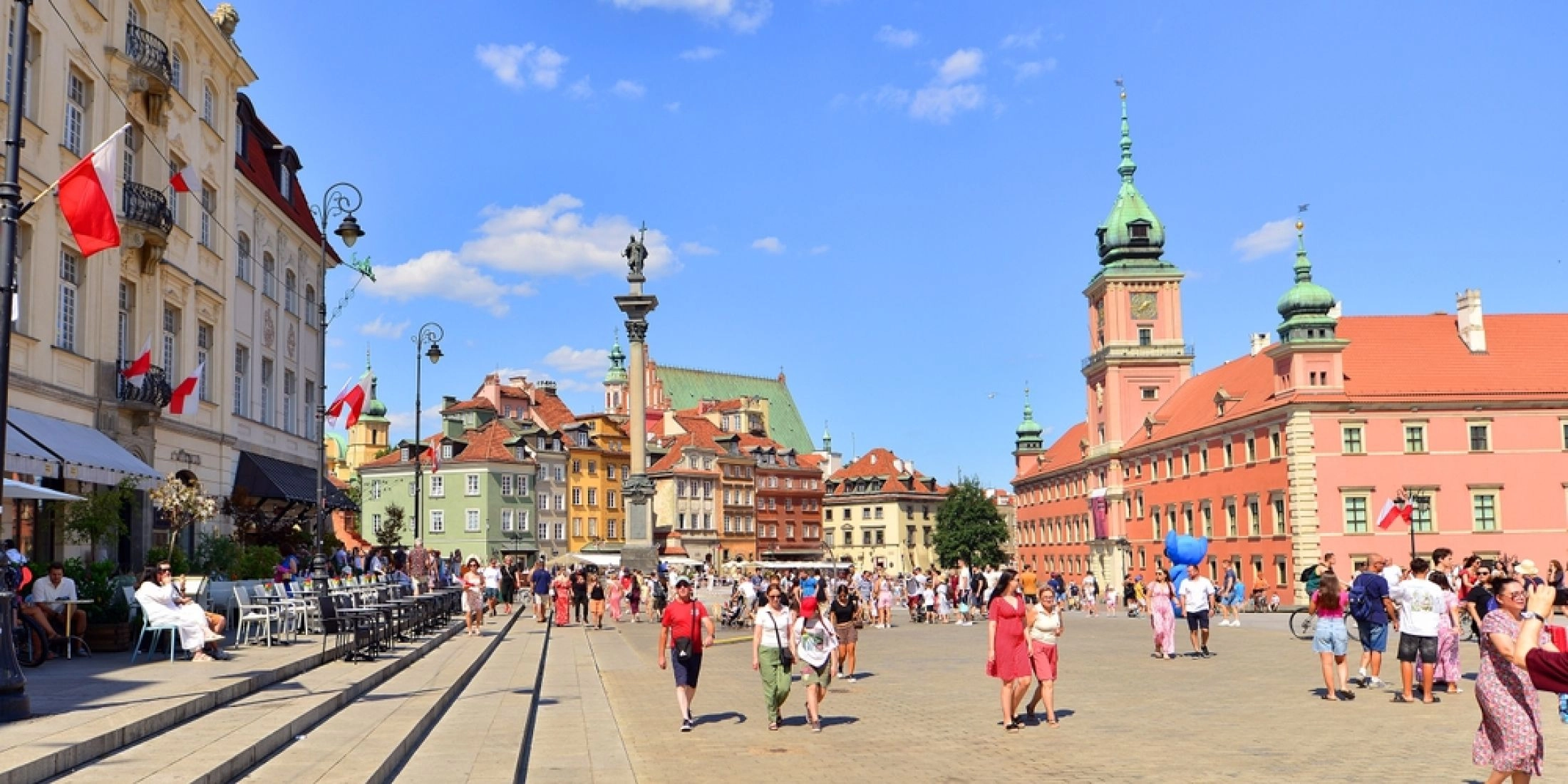 Plac Zamkowy i Stare Miasto w Warszawie w słoneczny dzień, spacerujący mieszkańcy i turyści.