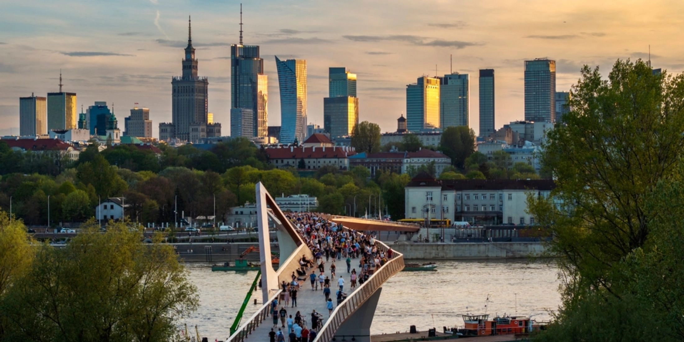 Kładka pieszo-rowerowa nad Wisłą w Warszawie, spacerujący ludzie i panorama miasta.