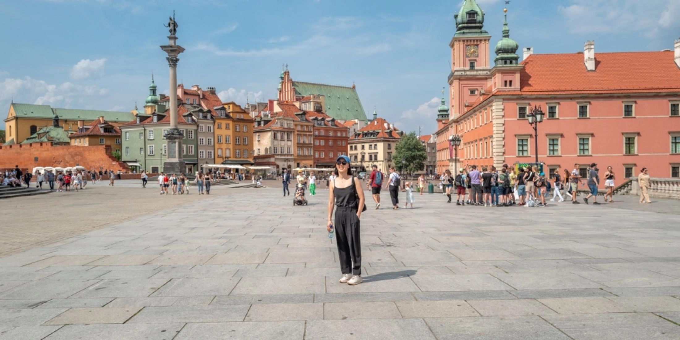 Plac Zamkowy w Warszawie z widokiem na Zamek Królewski, kolumnę Zygmunta i spacerujących turystów w majowy dzień.
