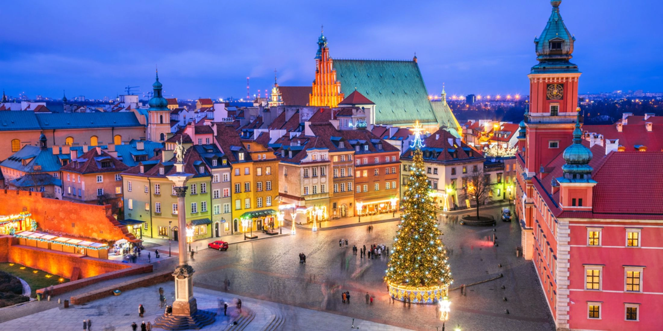 Rozświetlony Plac Zamkowy w Warszawie z choinką i zabytkowymi kamienicami nocą.