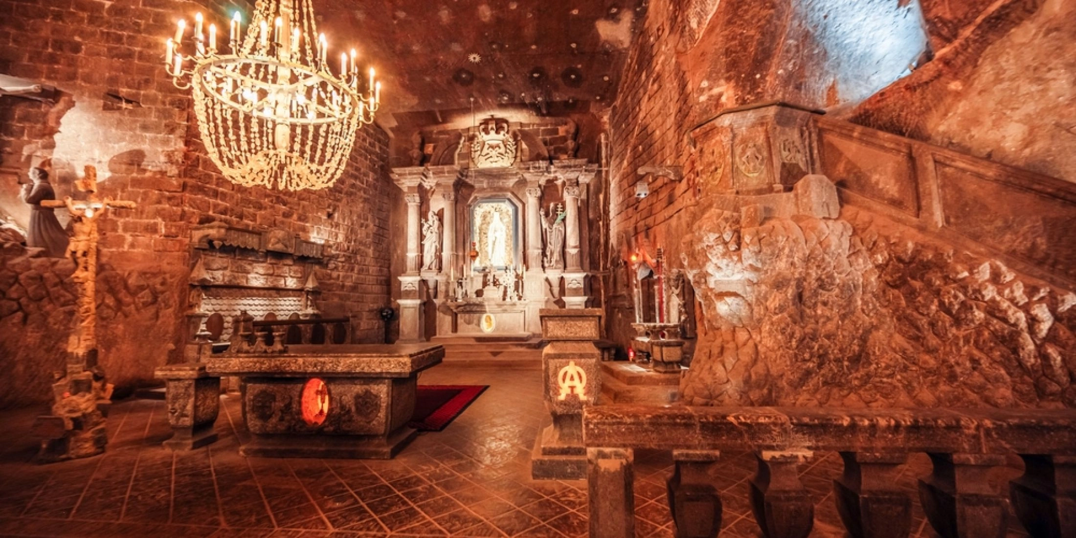 Wnętrze podziemnej kaplicy w Kopalni Soli Wieliczka z rzeźbionym ołtarzem, solnymi figurami i bogato zdobionym żyrandolem.