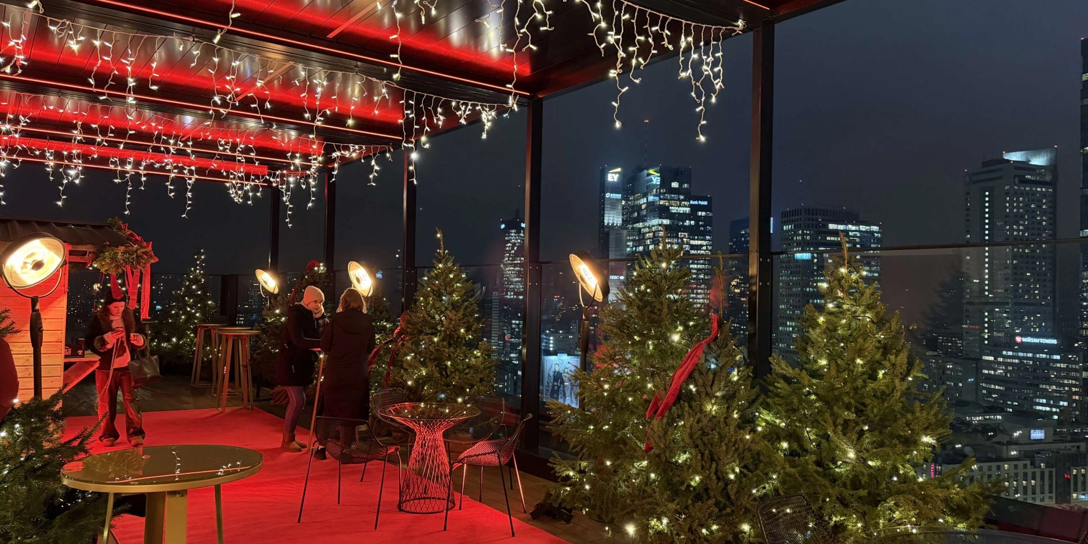 Zimowy taras Winter WOWderland na dachu NYX Hotel Warsaw, z choinkami, światełkami i panoramą Warszawy nocą.
