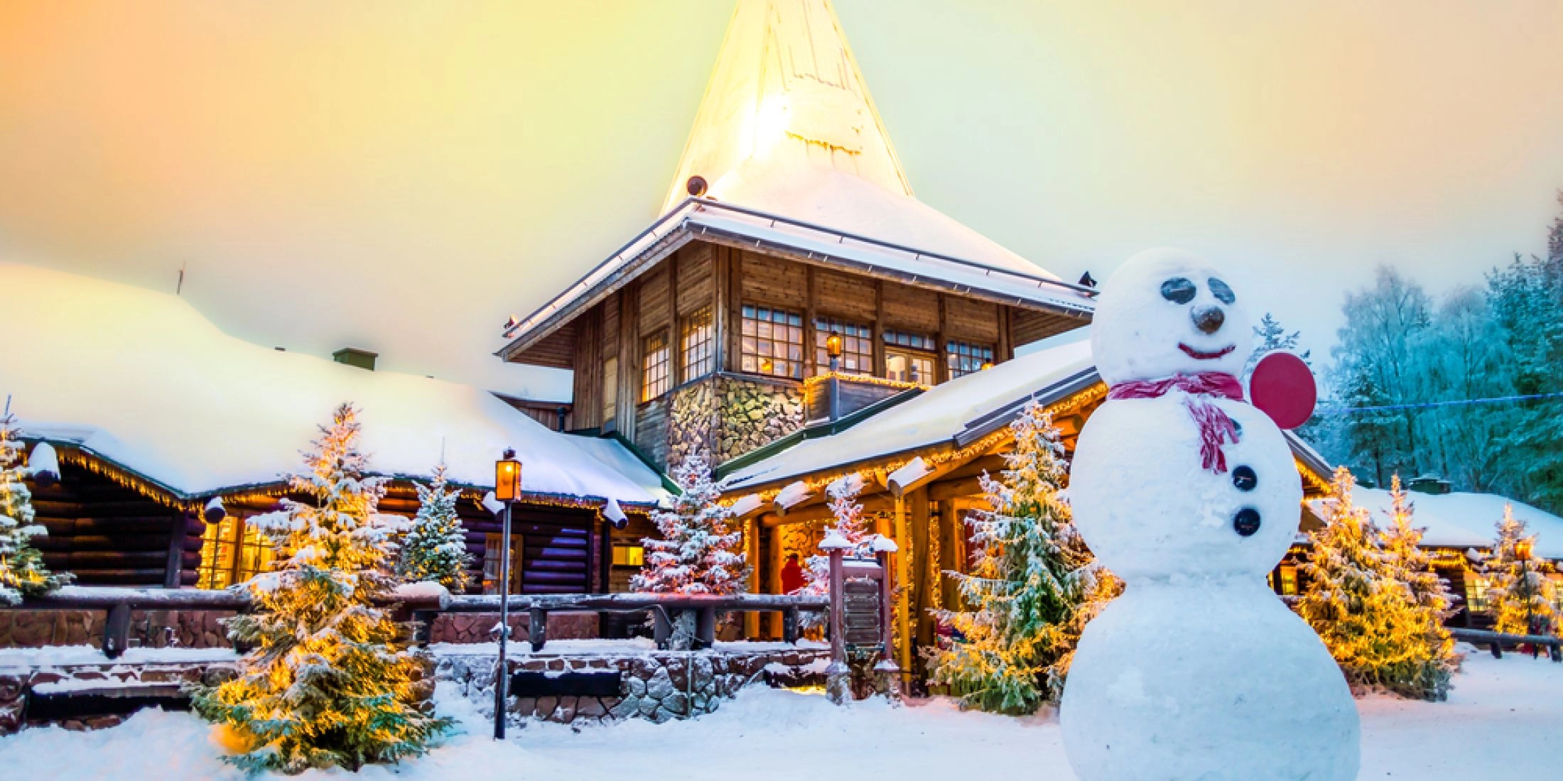 Drewniany dom w Santa Claus Village w Rovaniemi, ośnieżone choinki i ogromny bałwan przed wejściem.
