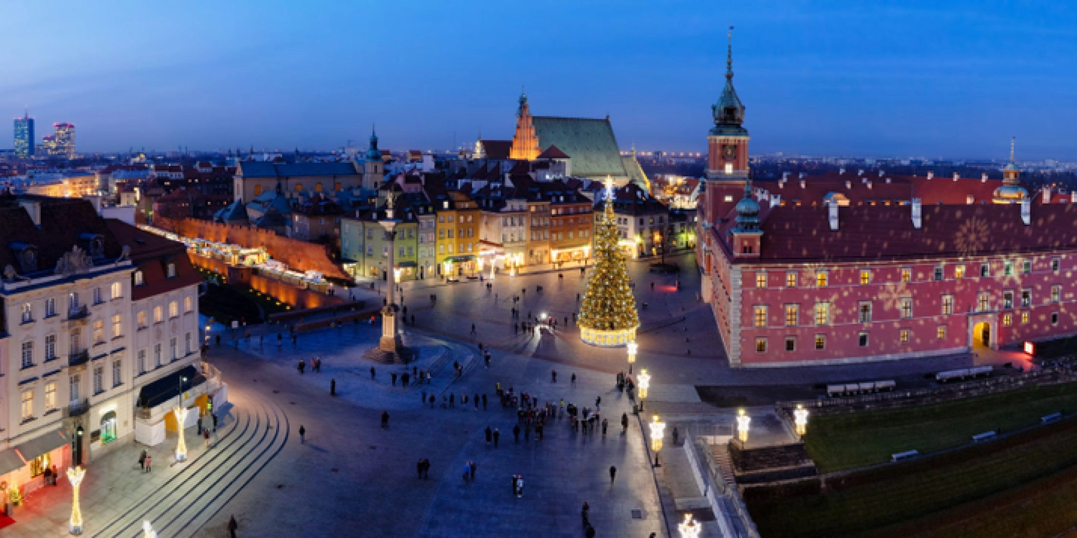 Panorama Placu Zamkowego i Starego Miasta w Warszawie o zmierzchu, z Zamkiem Królewskim, kolumną Zygmunta i oświetlonymi kamienicami zimą.