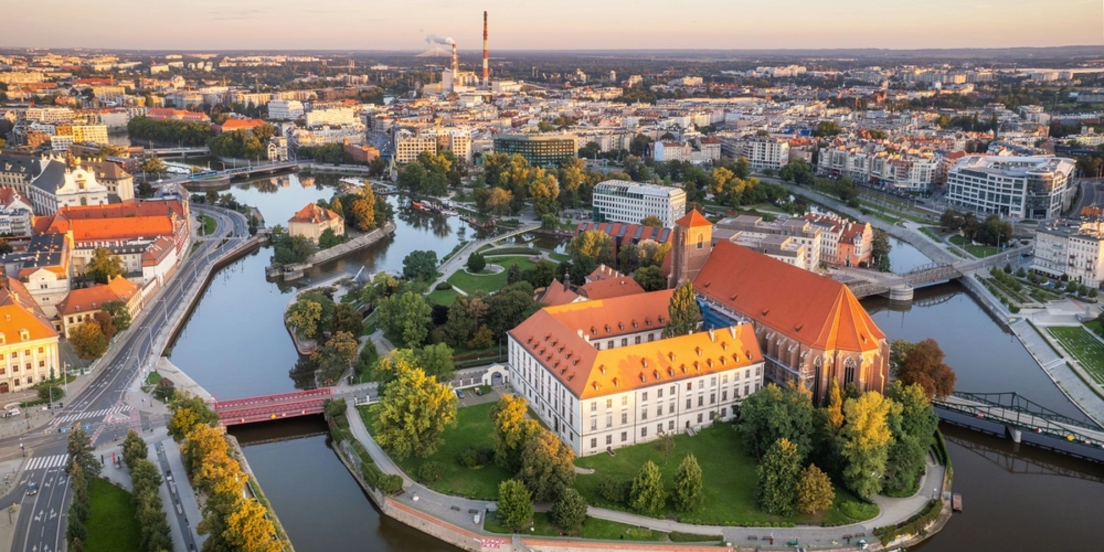 Widok z góry na wyspę otoczoną ramionami Odry, zabytkowy kościół, czerwone dachy, mosty i centrum Wrocławia.