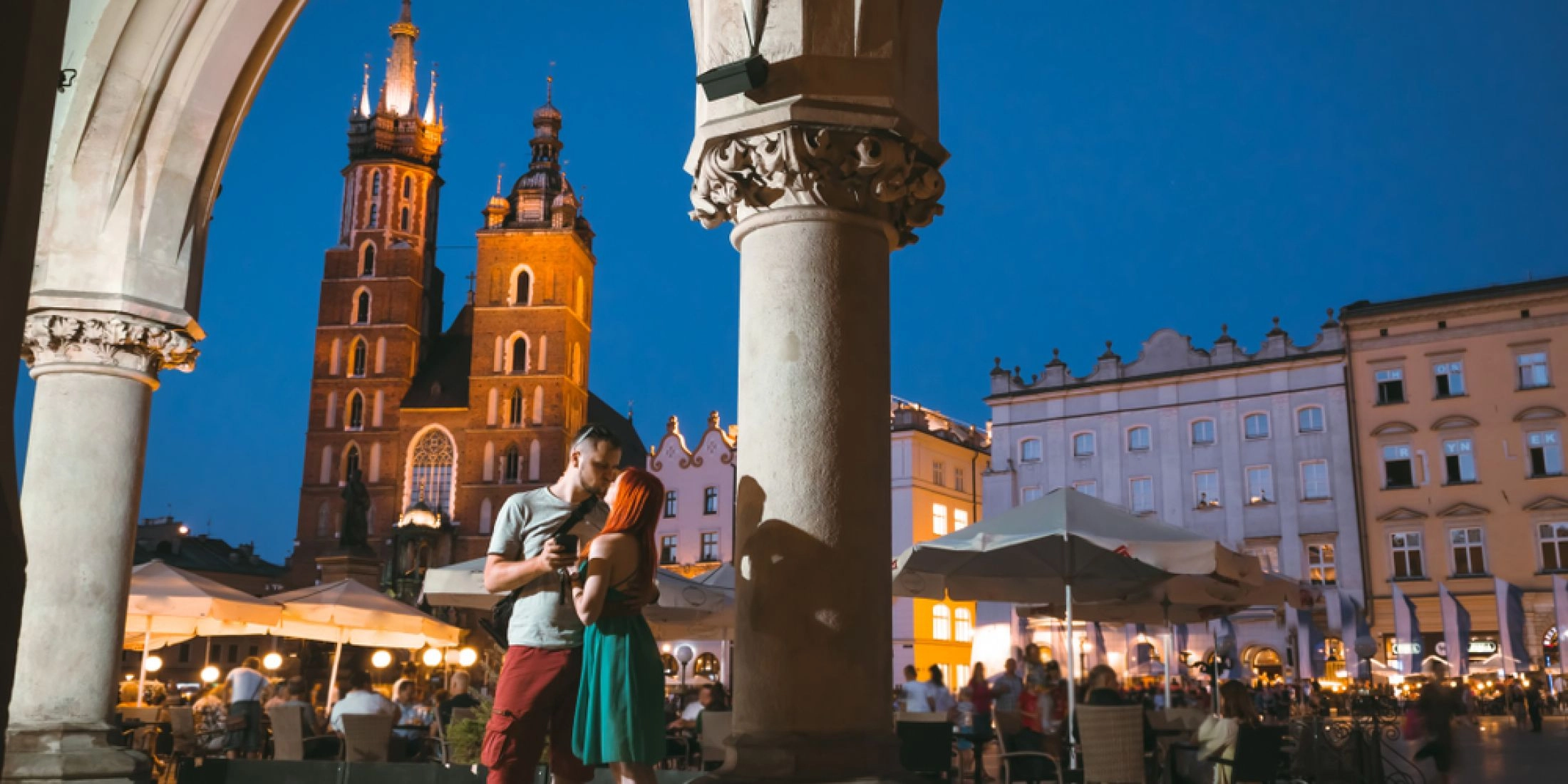 Para zakochanych na Rynku Głównym w Krakowie o zmroku, w tle Kościół Mariacki