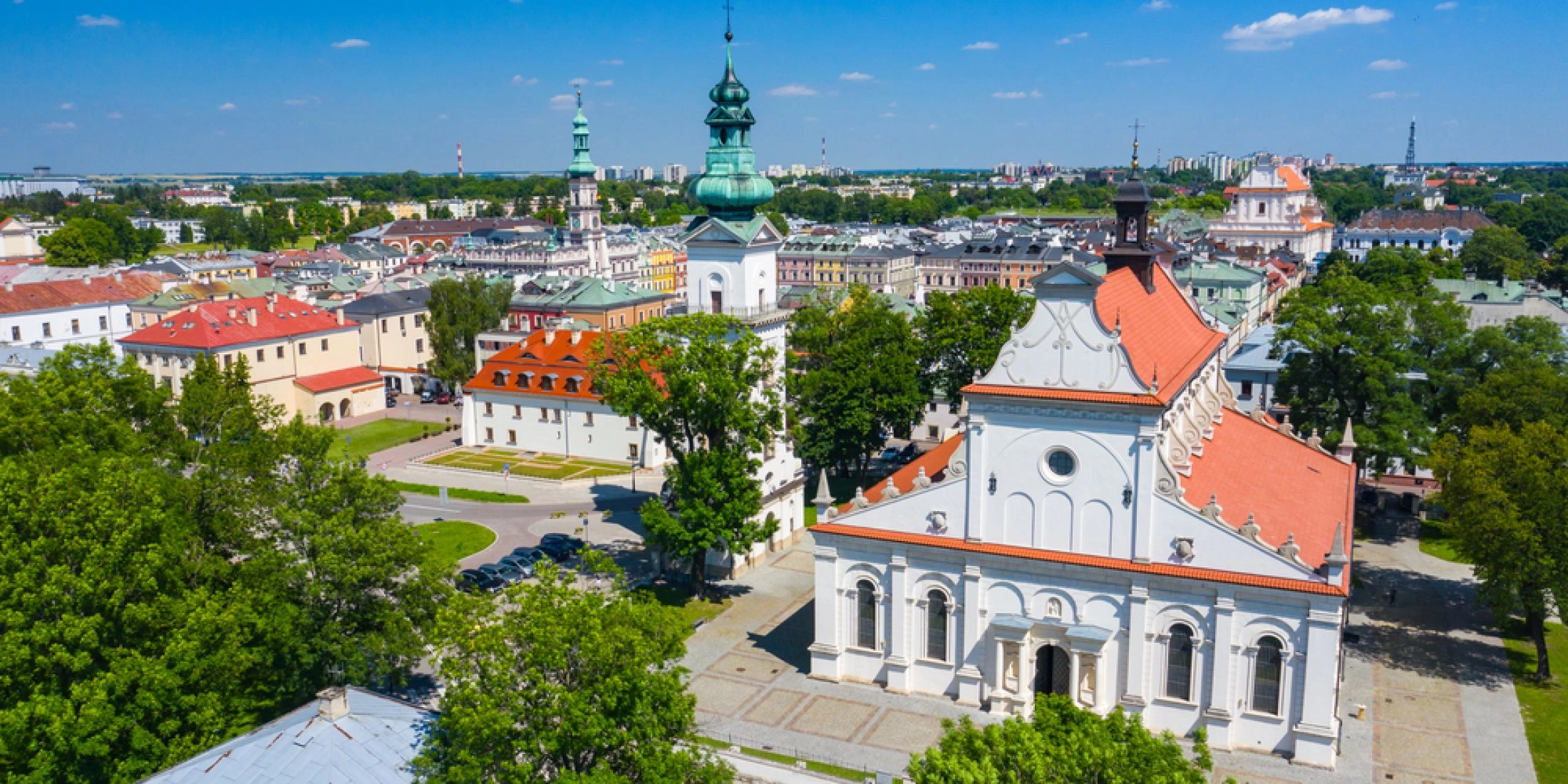 Panorama zabytkowego centrum Zamościa z lotu ptaka, z kościołem o czerwonym dachu, wieżami i historyczną zabudową miasta.